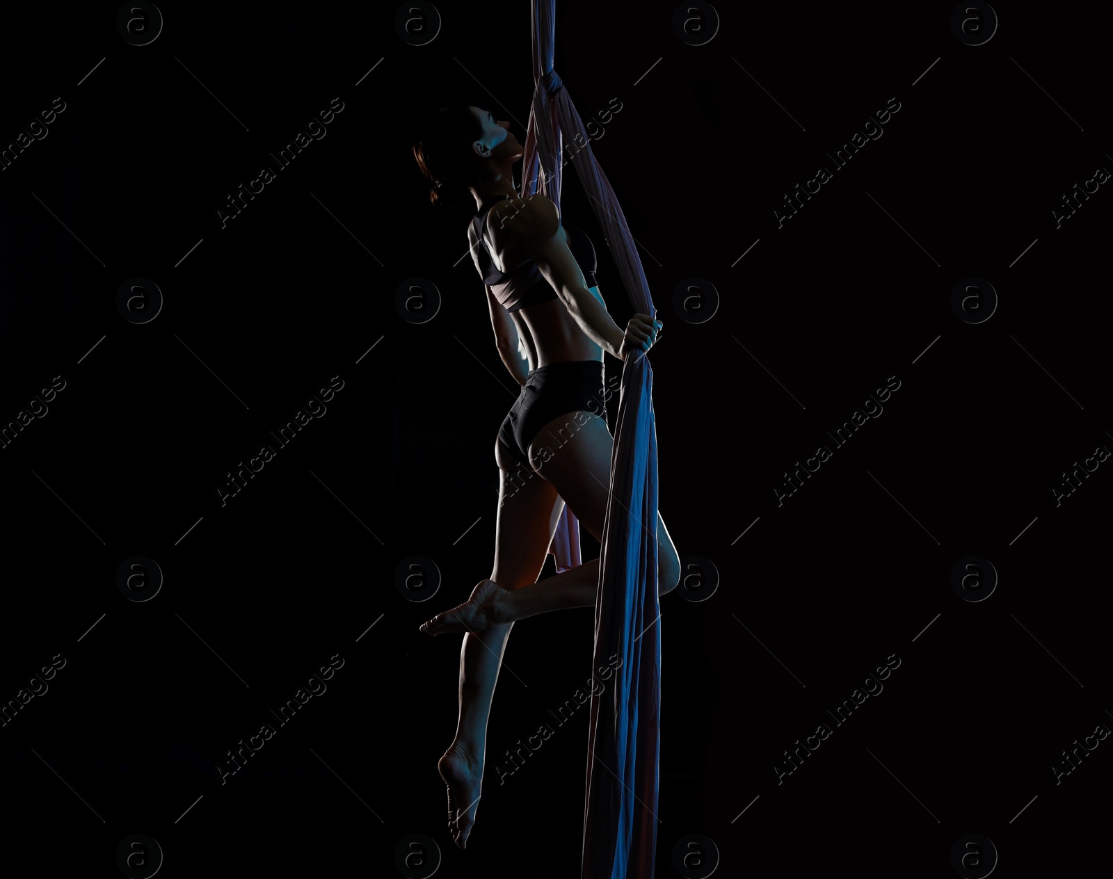 Photo of Young woman performing acrobatic element on aerial silk indoors