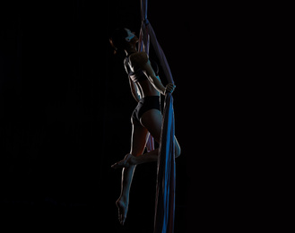 Photo of Young woman performing acrobatic element on aerial silk indoors