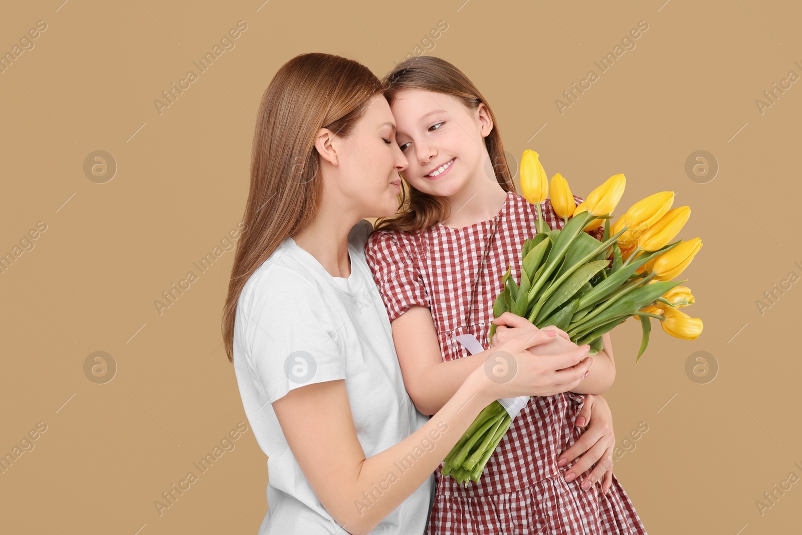 Photo of Mother and her cute daughter with bouquet of yellow tulips on beige background