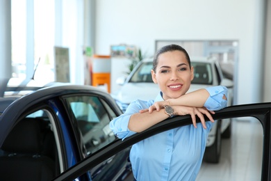 Young saleswoman near automobile in car dealership