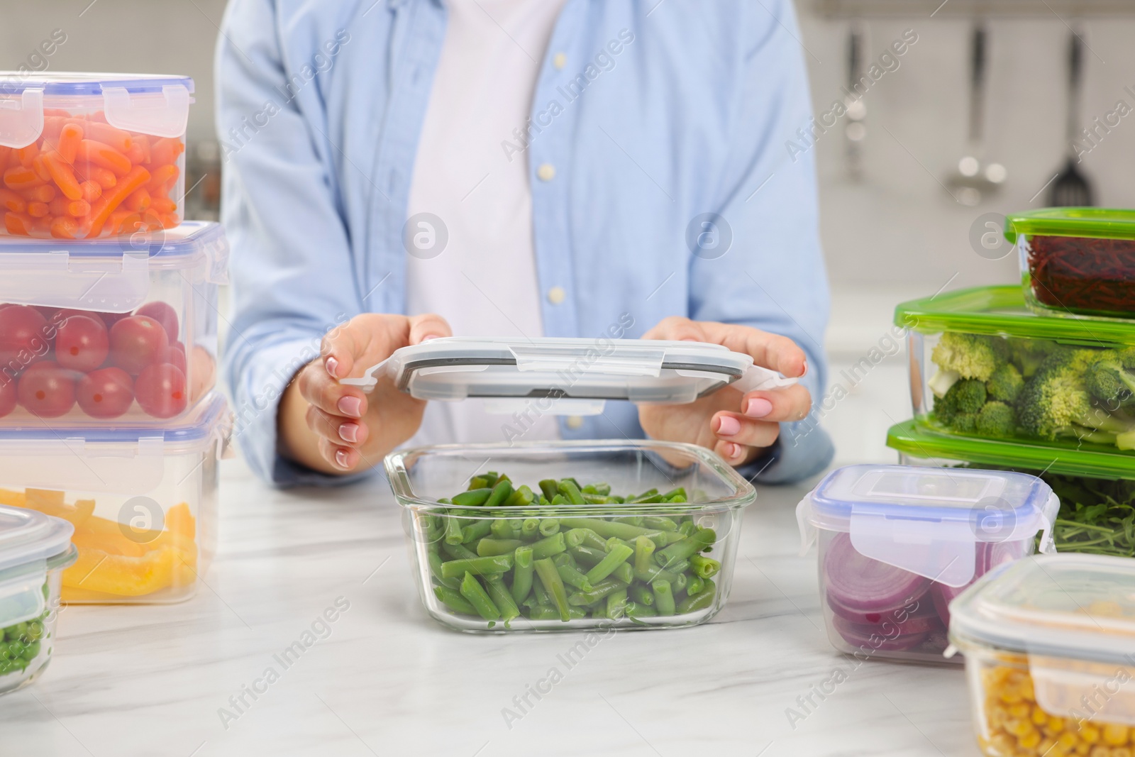 Photo of Woman sealing container with green beans at white marble table in kitchen, closeup. Food storage