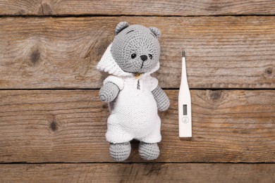 Photo of Toy bear and thermometer on wooden background, flat lay
