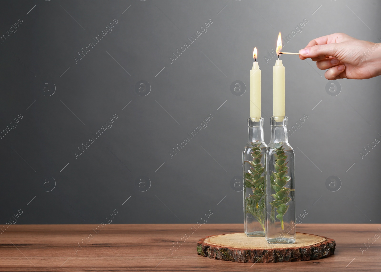 Photo of Woman lighting candle on wooden table, closeup. Space for text