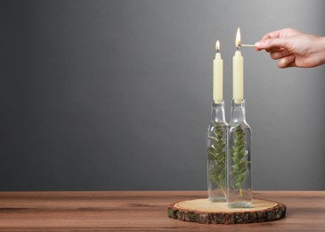 Photo of Woman lighting candle on wooden table, closeup. Space for text