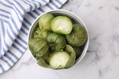 Photo of Fresh green tomatillos with husk in bowl on light marble table, top view