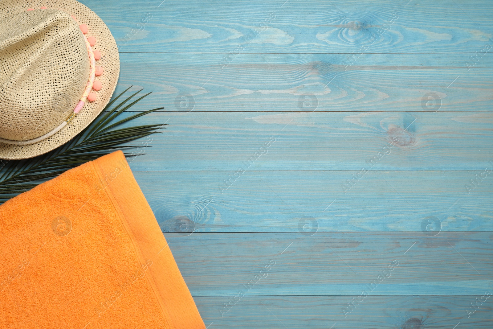 Photo of Beach towel and straw hat on light blue wooden background, flat lay. Space for text