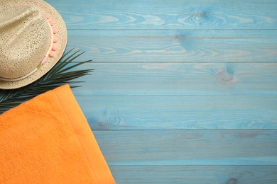 Beach towel and straw hat on light blue wooden background, flat lay. Space for text