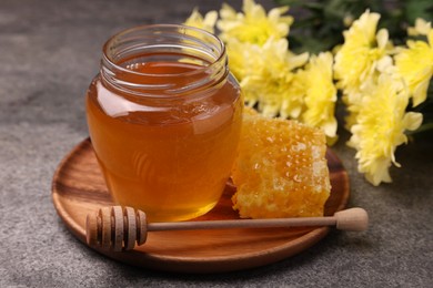 Photo of Sweet golden honey in jar, dipper and honeycomb on grey textured table, closeup