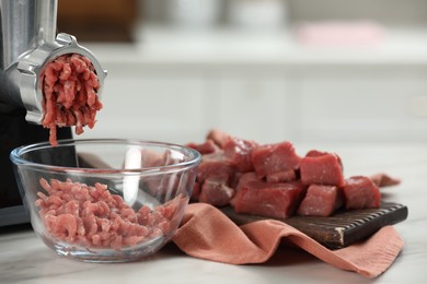 Electric meat grinder with beef mince on white table against blurred background, selective focus. Space for text