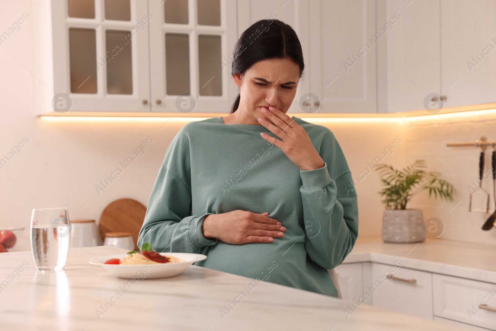 Photo of Young woman feeling nausea while seeing food at table in kitchen. Toxicosis during pregnancy