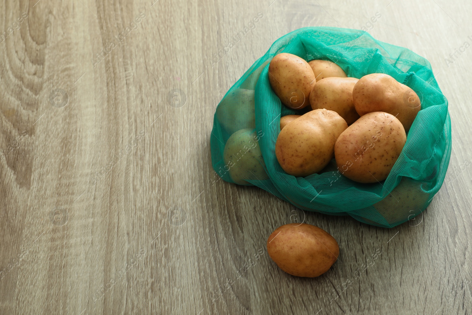 Photo of Net bag with potatoes on wooden table. Space for text