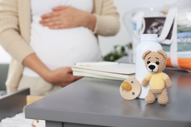 Pregnant woman at home, focus on pacifier, bottle and bear toy
