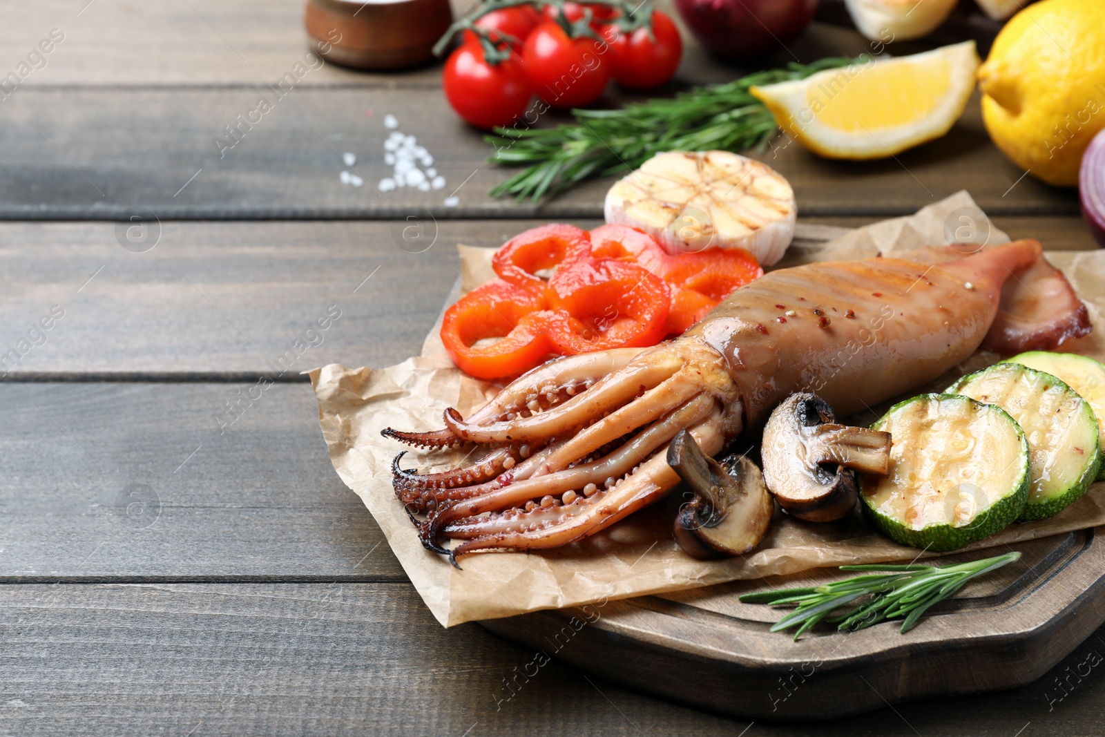 Photo of Tasty grilled squid with vegetables served on wooden table, space for text