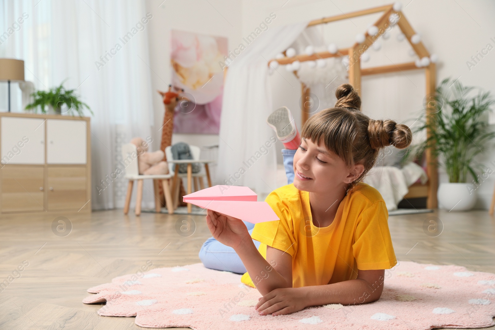 Photo of Cute little girl playing with paper plane on floor in room. Space for text
