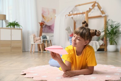 Cute little girl playing with paper plane on floor in room. Space for text