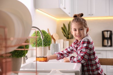 Little girl washing dishes in kitchen at home