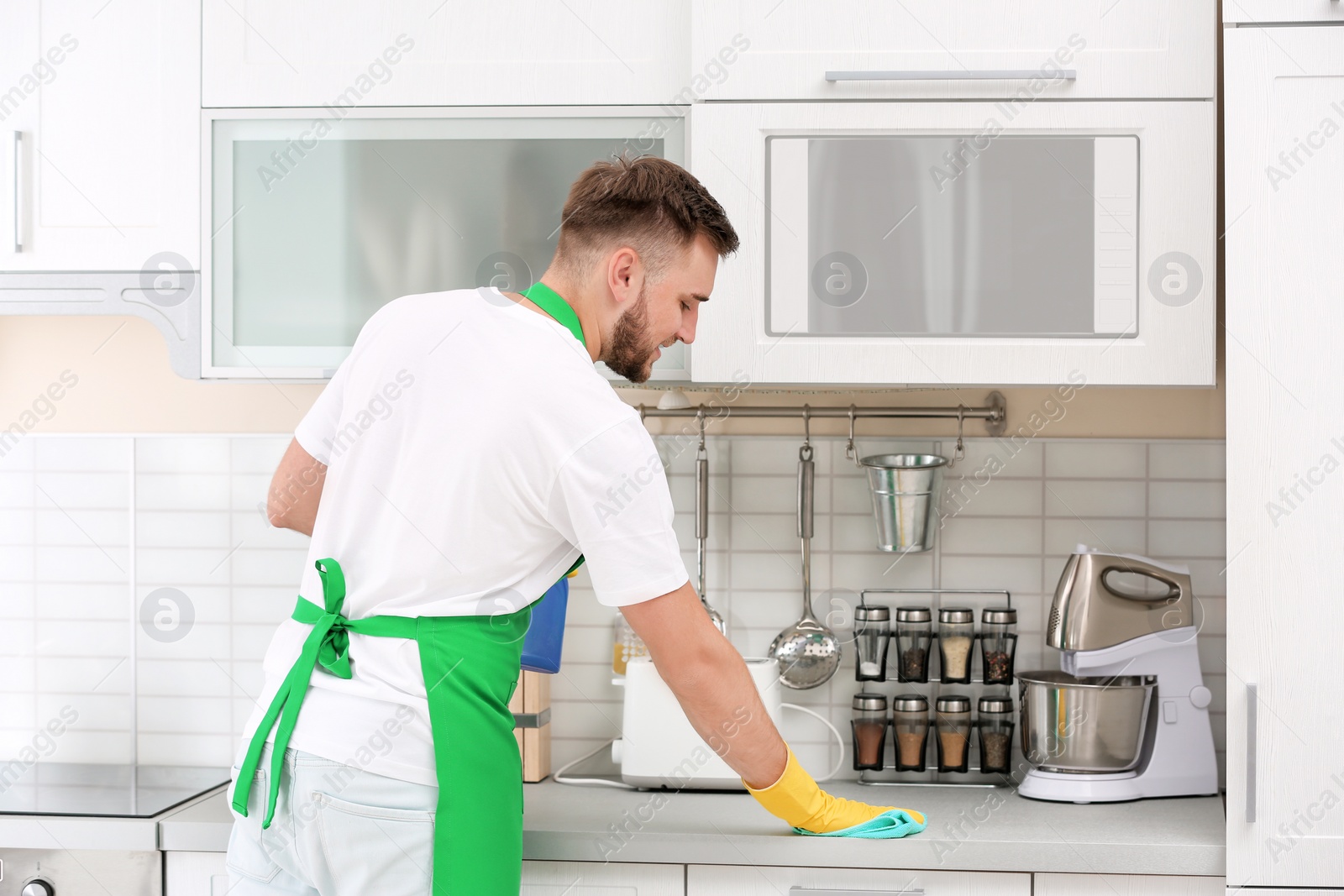 Photo of Young man in uniform cleaning kitchen counter