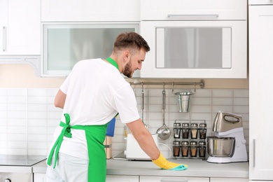 Photo of Young man in uniform cleaning kitchen counter