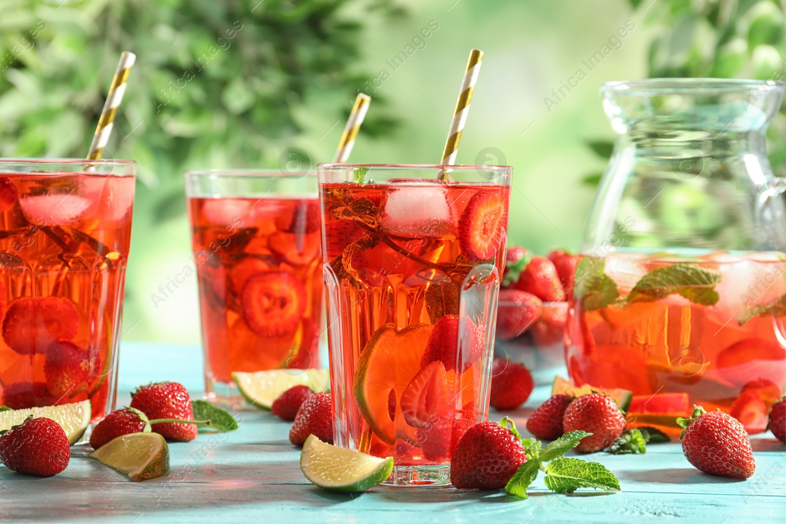 Photo of Refreshing drink with strawberry and lime on light blue wooden table