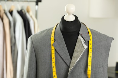 Photo of Mannequin with unfinished jacket and measuring tape in tailor shop, closeup