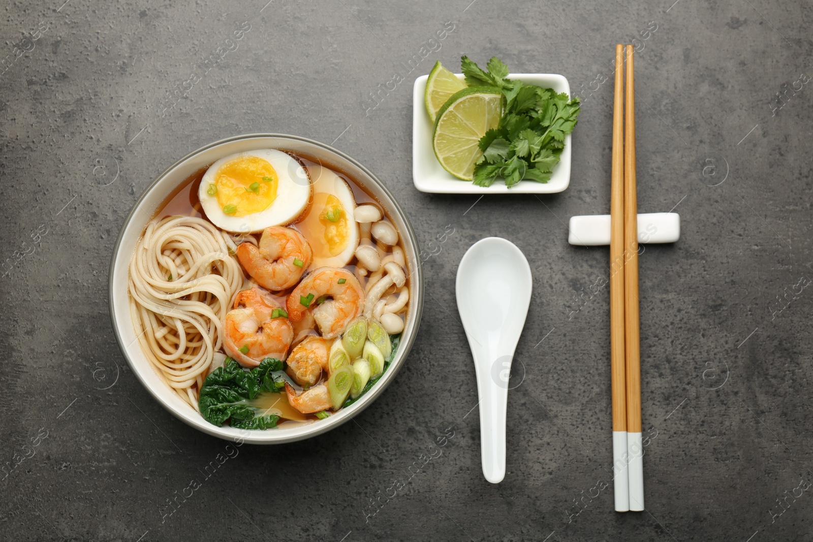 Photo of Delicious ramen with shrimps and egg in bowl served on grey table, flat lay. Noodle soup