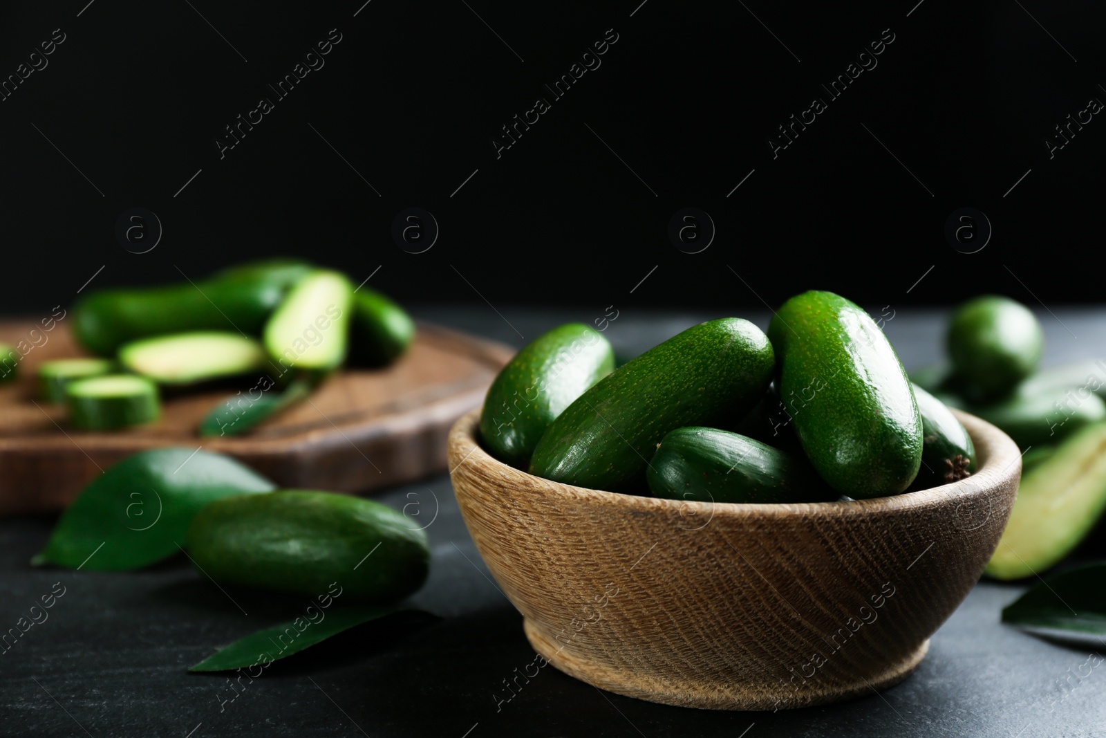 Photo of Fresh seedless avocados with green leaves in wooden bowl on grey table. Space for text