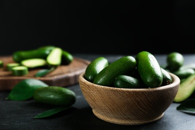 Photo of Fresh seedless avocados with green leaves in wooden bowl on grey table. Space for text
