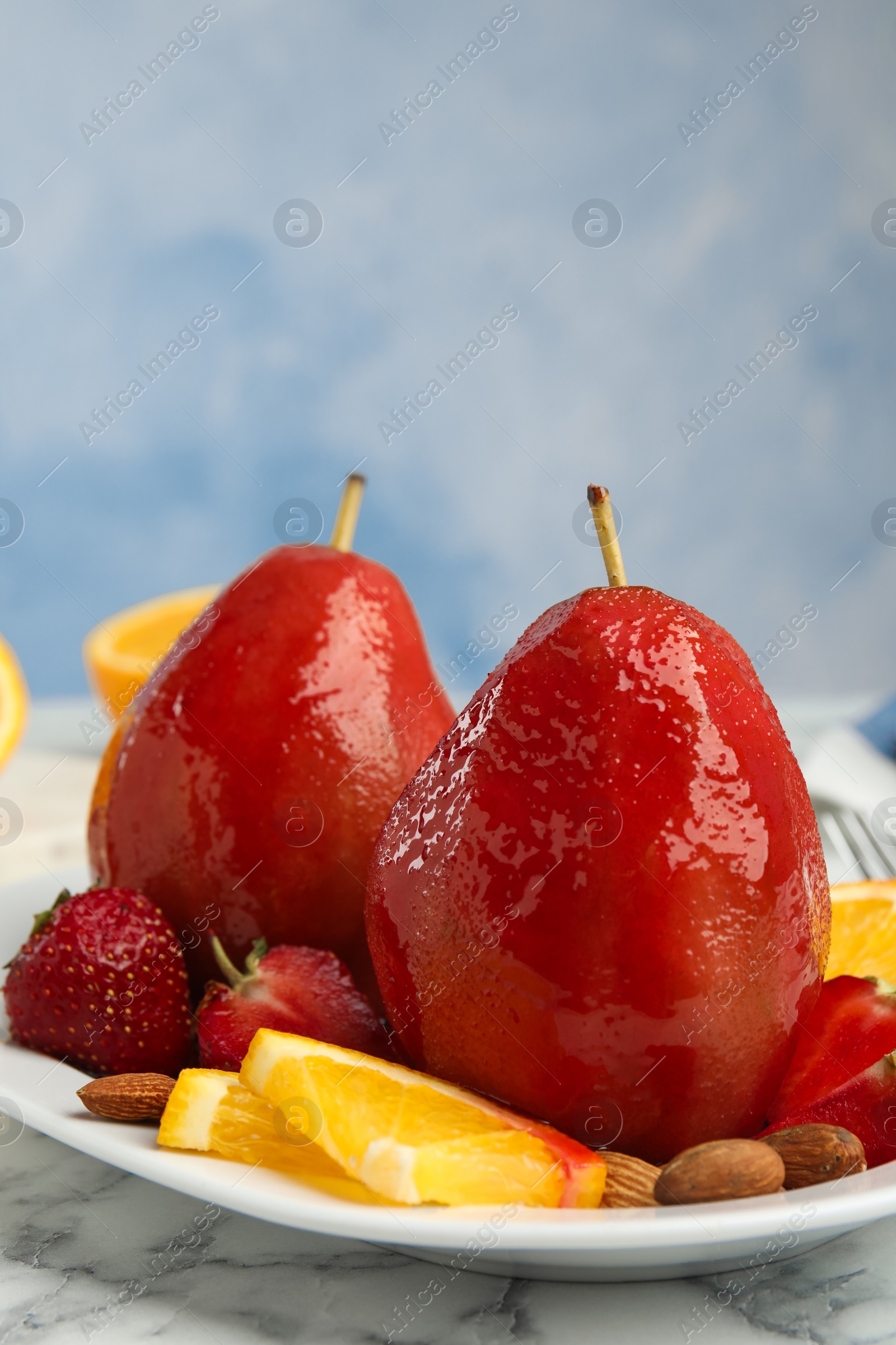 Photo of Plate with red wine poached pears and fruits on marble table against blue background. Space for text