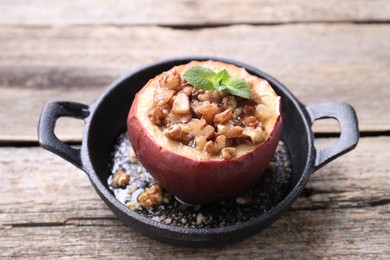 Photo of Tasty baked apple with nuts, honey and mint in baking dish on wooden table