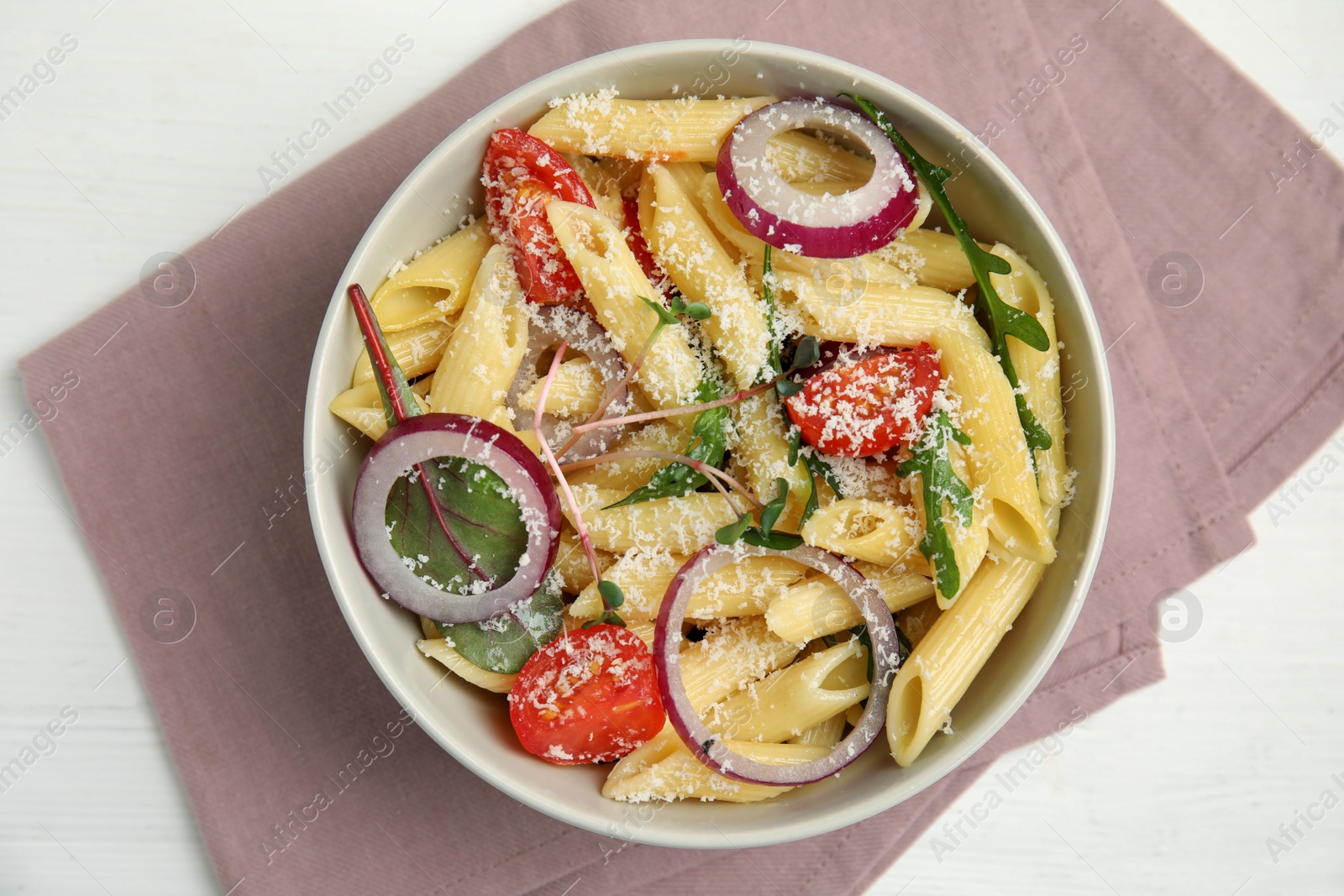 Photo of Bowl of delicious pasta with tomatoes, onion and cheese on white wooden table, top view