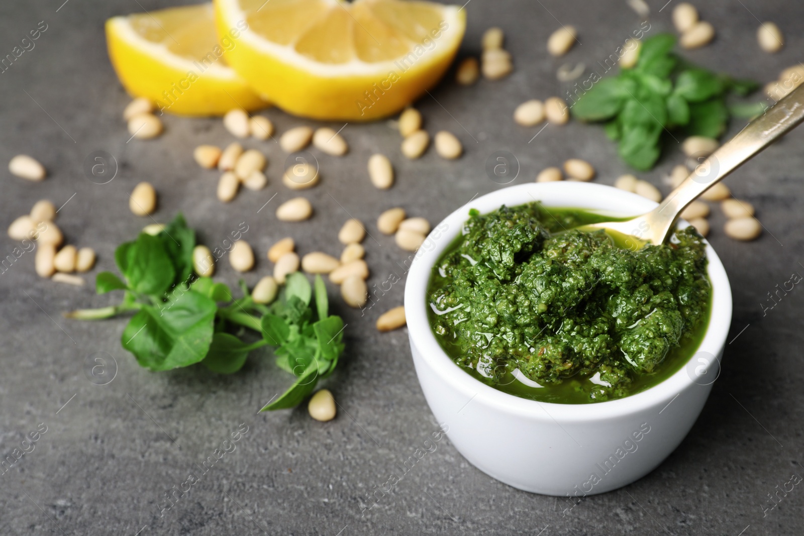 Photo of Homemade basil pesto sauce in bowl and ingredients on table