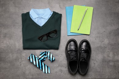 Stylish school uniform for boy and stationery on grey background, flat lay