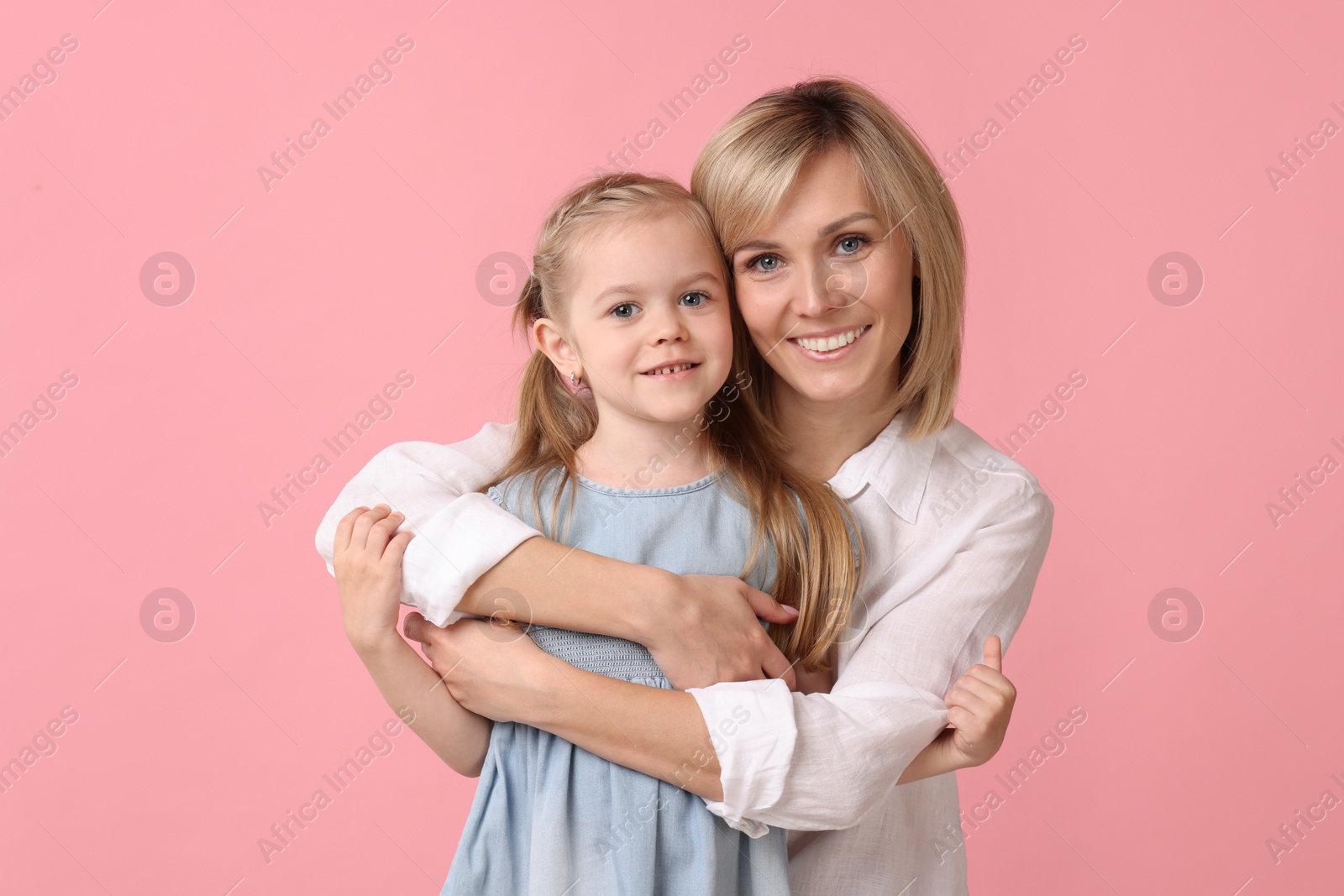 Photo of Mother hugging her happy daughter on pink background