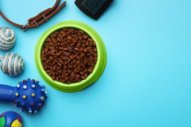 Photo of Pet toys, bowl of food and accessories on light blue background, flat lay. Space for text
