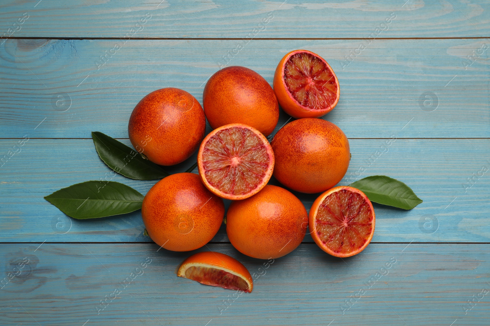 Photo of Many ripe sicilian oranges and leaves on light blue wooden table, flat lay