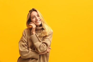 Photo of Beautiful young woman wearing knitted sweater on yellow background. Space for text