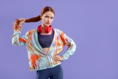 Photo of Young woman in sportswear and headphones on violet background, space for text