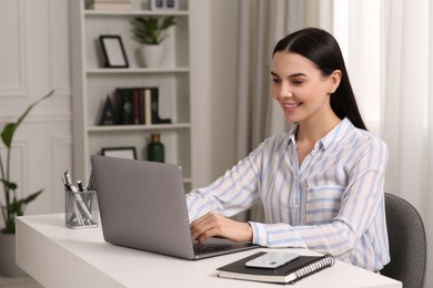 Happy woman working with laptop at white desk in room