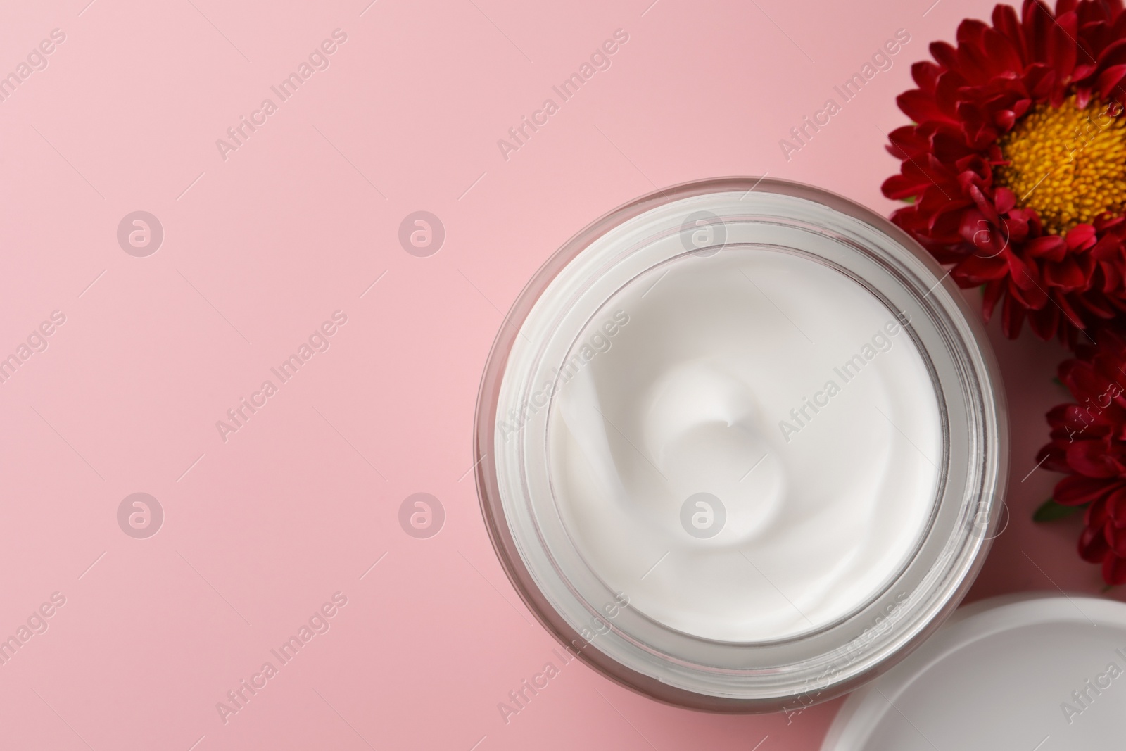 Photo of Jar of face cream and chrysanthemum flowers on pink background, flat lay. Space for text