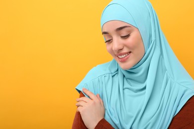 Portrait of Muslim woman in hijab on orange background, space for text