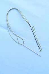 Photo of Sewing needle with thread and stitches on light blue cloth, top view