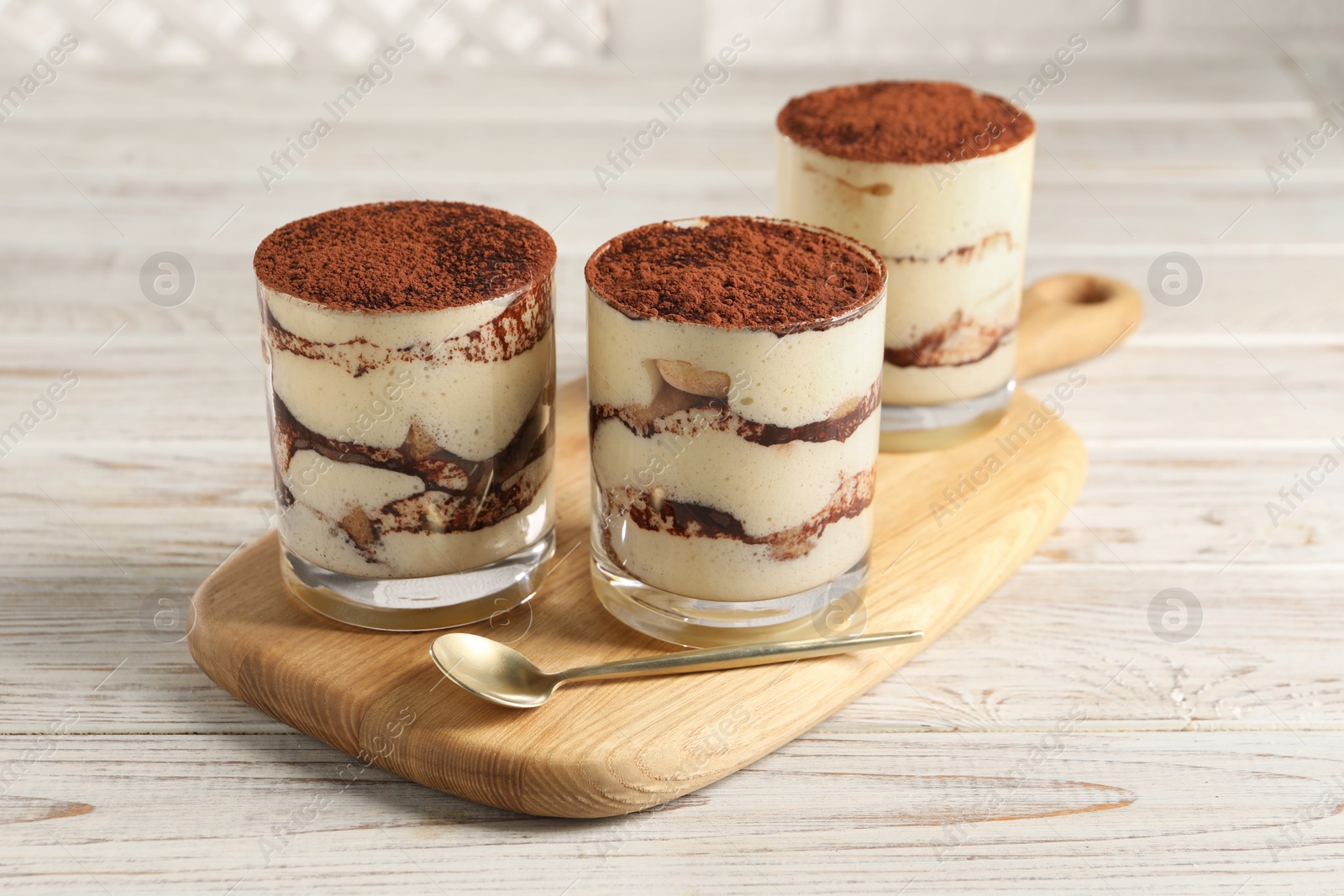 Photo of Delicious tiramisu in glasses and spoon on light wooden table