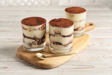 Delicious tiramisu in glasses and spoon on light wooden table