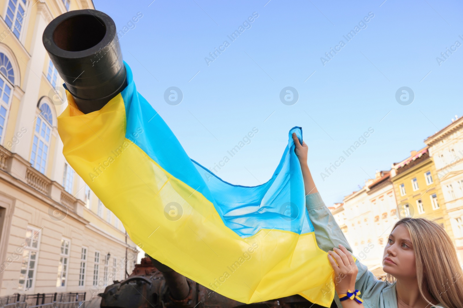 Photo of Sad woman holding Ukrainian flag near broken tank in city