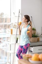 Photo of Young woman in fitness clothes with glass of juice at home