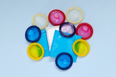 Photo of Unpacked condoms and packages on light blue background, top view. Safe sex