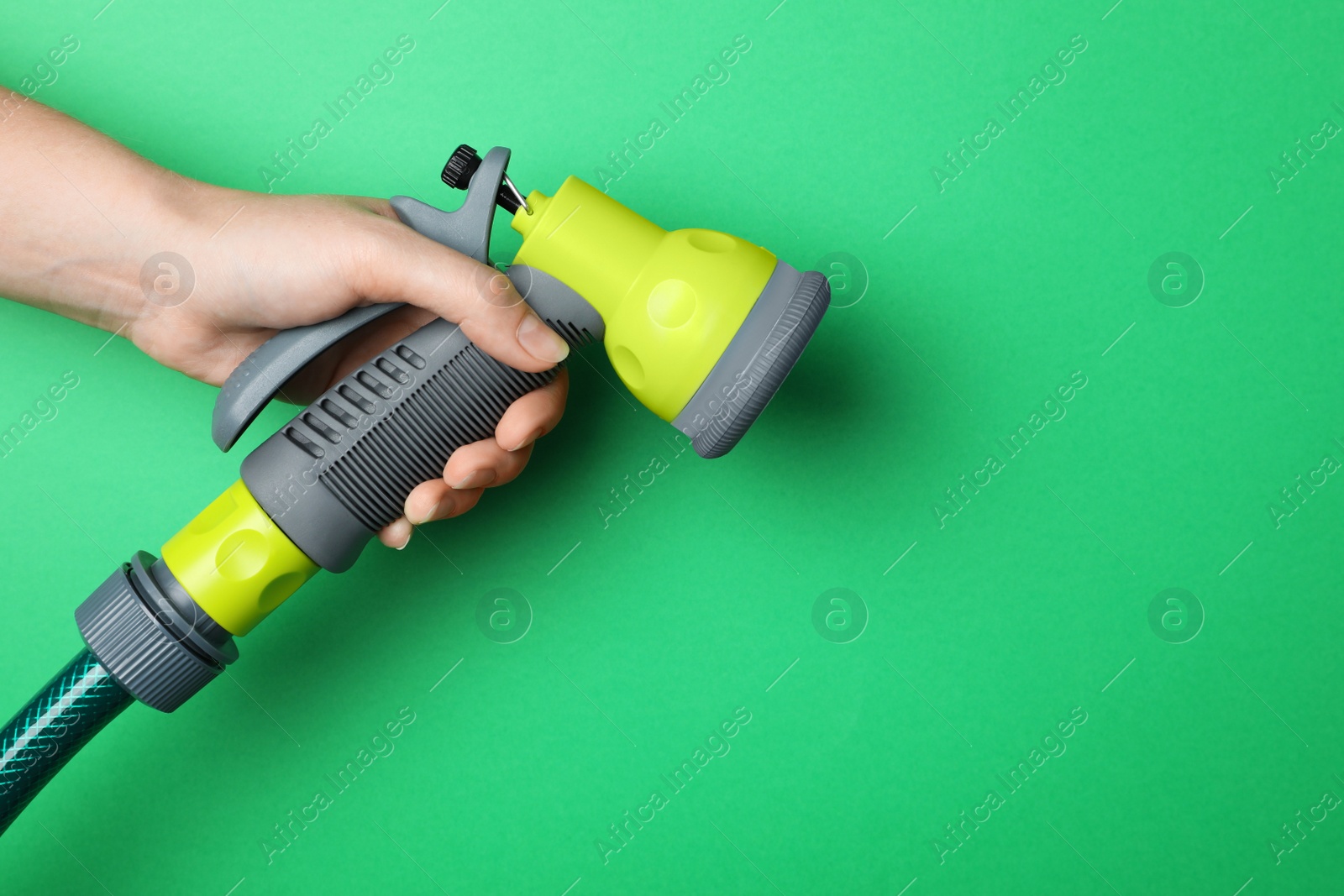 Photo of Woman holding watering hose with sprinkler on green background, closeup. Space for text