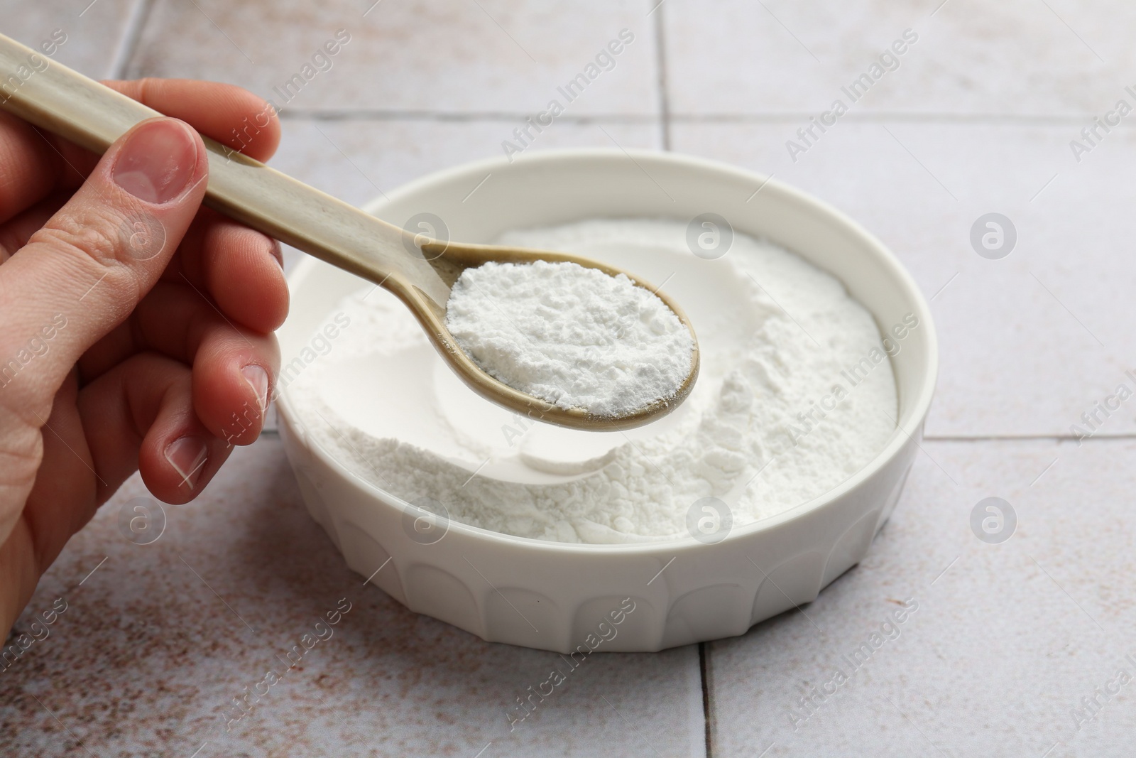 Photo of Woman taking baking powder with spoon from bowl at light tiled table, closeup