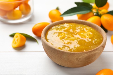 Photo of Delicious kumquat jam in bowl and fresh fruits on white wooden table, space for text