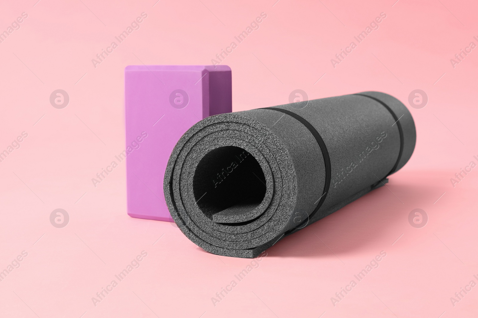 Photo of Grey exercise mat and yoga block on pink background